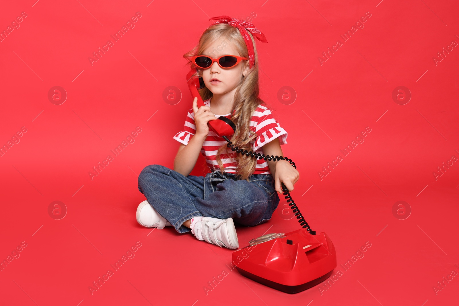 Photo of Cute little girl with telephone on red background