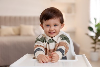 Photo of Cute little kid sitting in high chair at home