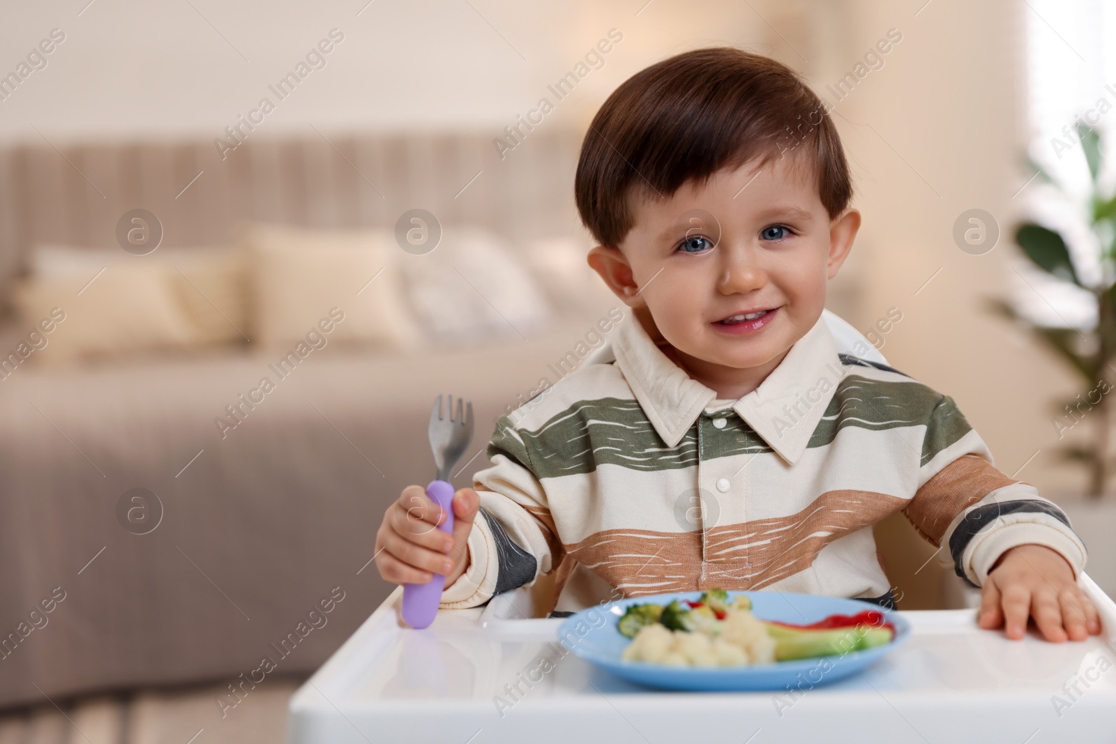 Photo of Cute little baby eating healthy food in high chair at home