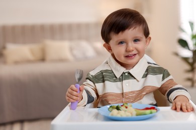 Photo of Cute little baby eating healthy food in high chair at home