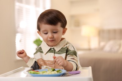 Photo of Cute little baby eating healthy food in high chair at home