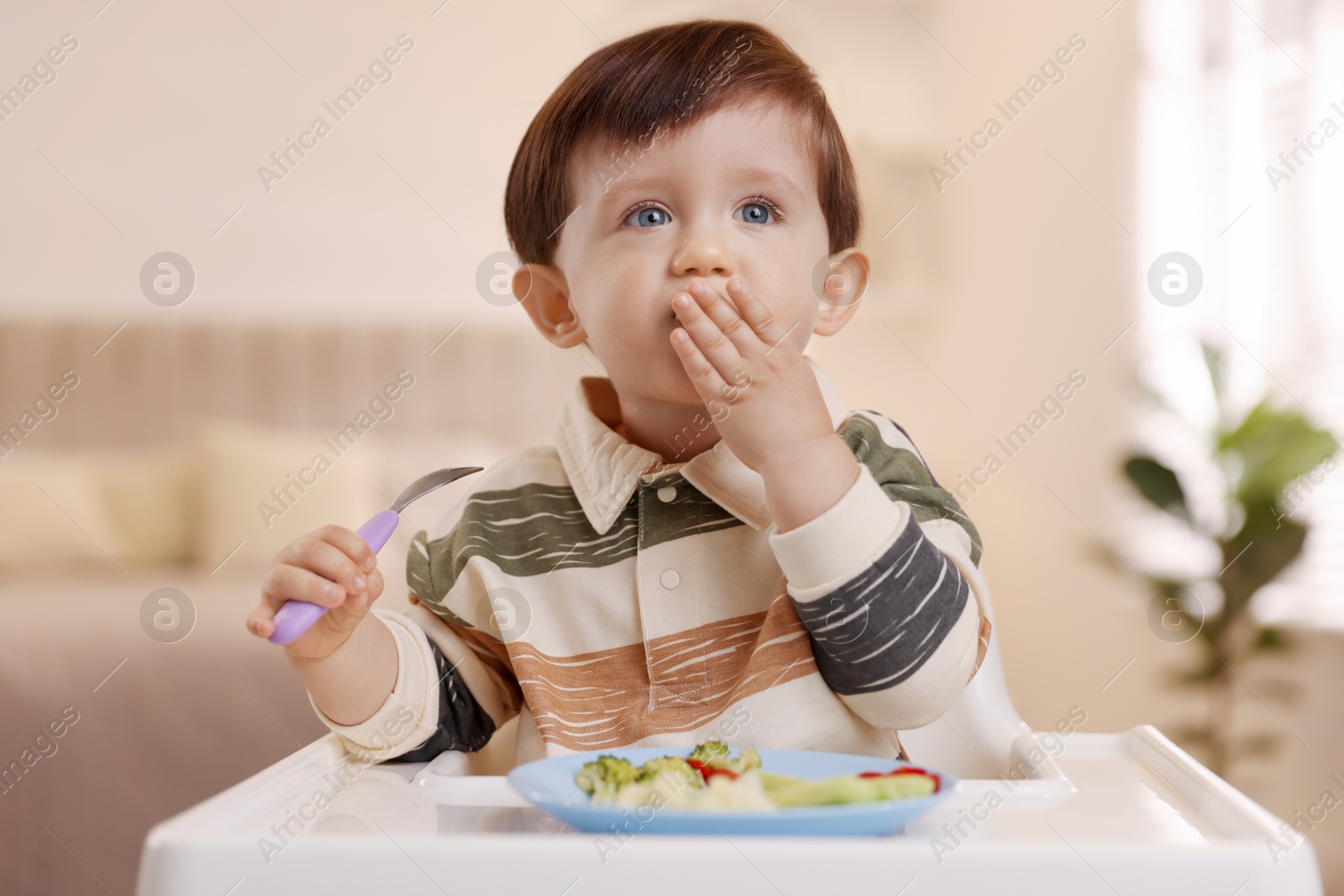 Photo of Cute little baby eating healthy food in high chair at home