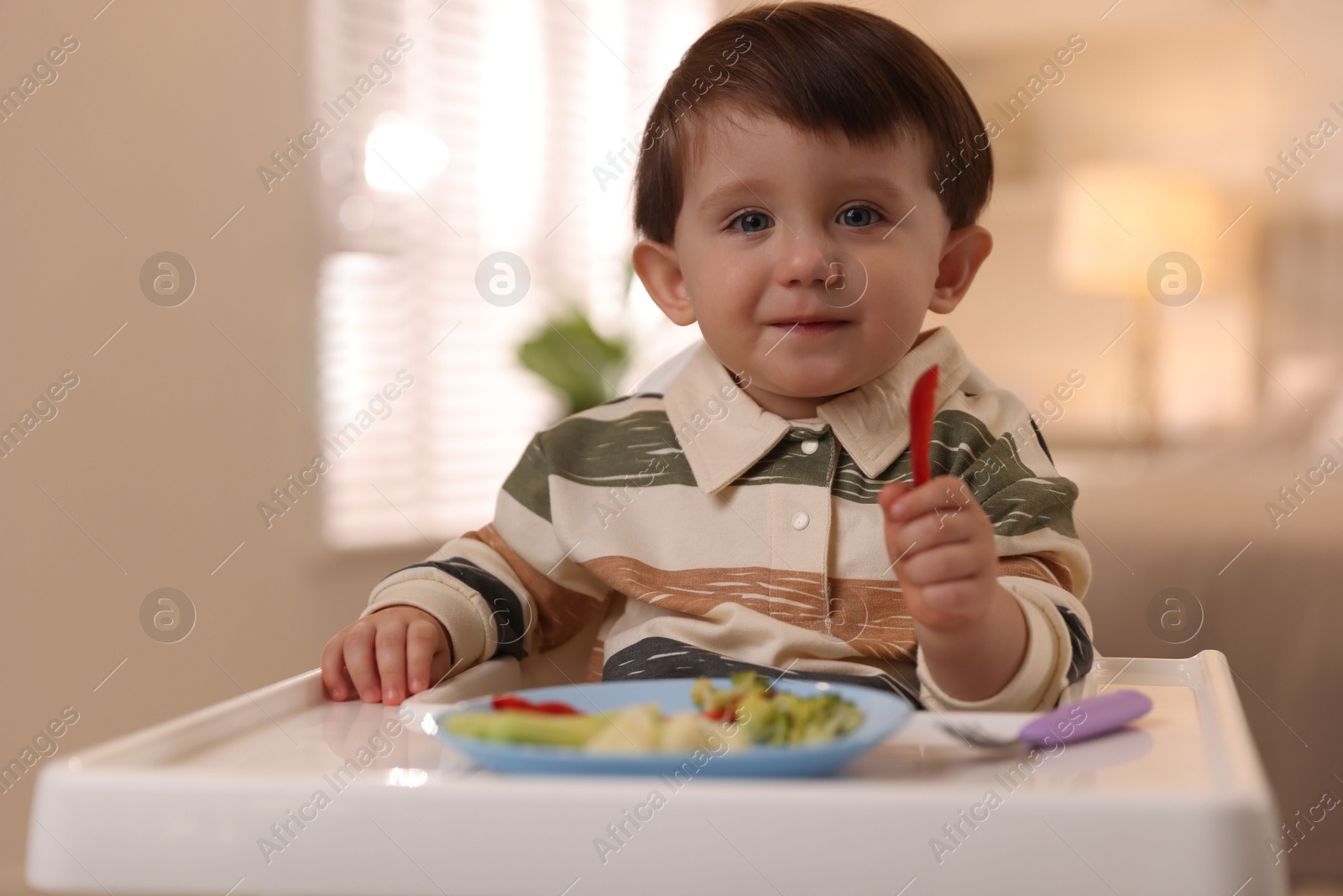 Photo of Cute little baby eating healthy food in high chair at home