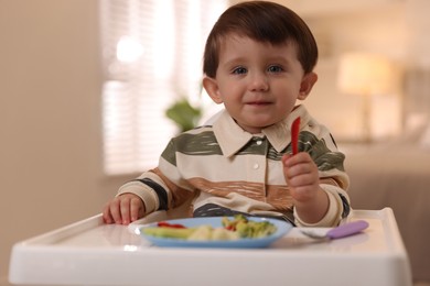 Photo of Cute little baby eating healthy food in high chair at home