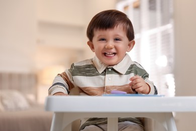 Photo of Cute little baby eating healthy food in high chair at home