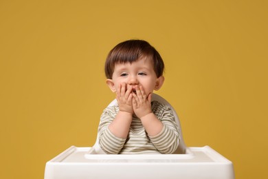 Photo of Cute little kid sitting in high chair on yellow background