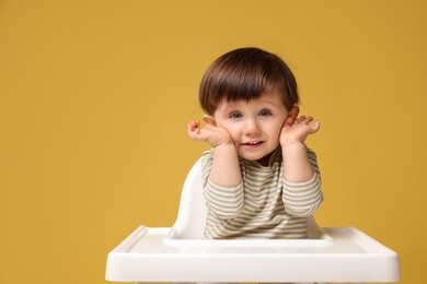 Photo of Cute little kid sitting in high chair on yellow background