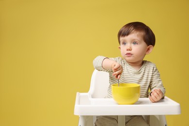 Photo of Cute little kid eating healthy baby food from bowl in high chair on yellow background, space for text