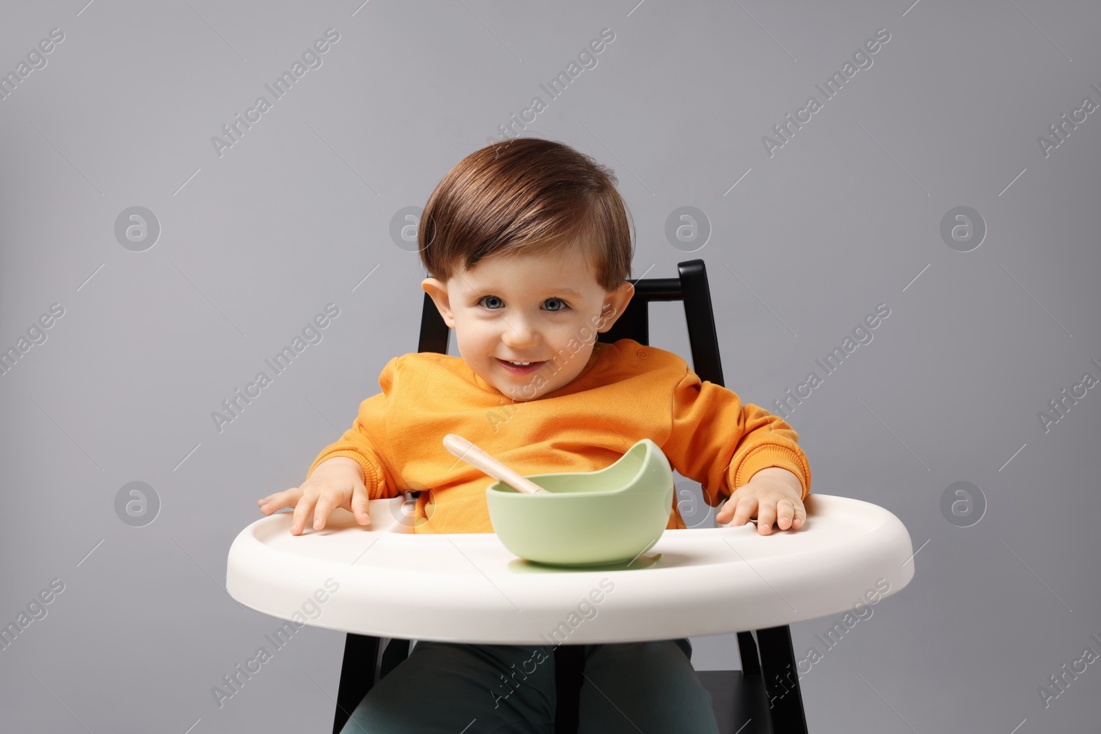 Photo of Cute little kid eating healthy baby food from bowl in high chair on light grey background