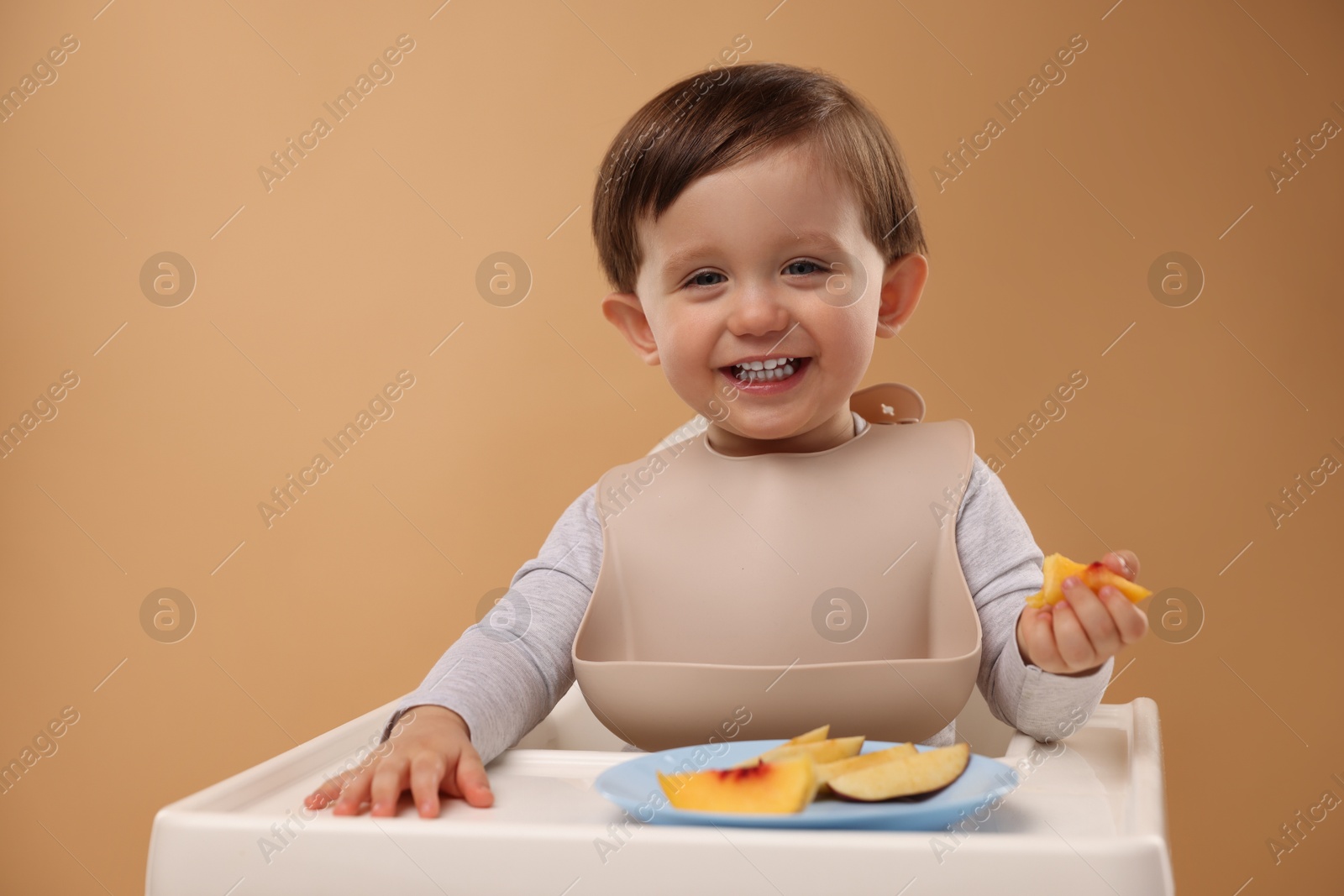 Photo of Healthy baby food. Cute little kid eating fruits in high chair on beige background