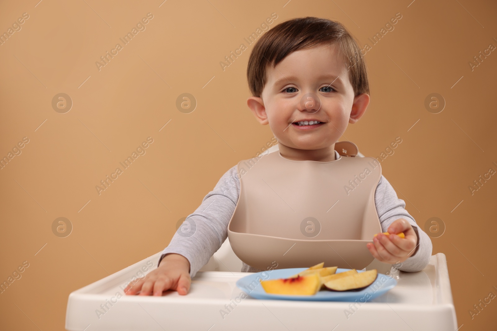 Photo of Healthy baby food. Cute little kid eating fruits in high chair on beige background