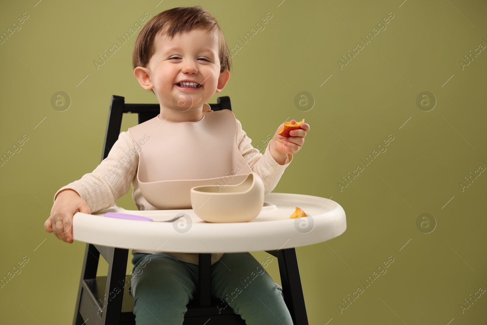 Photo of Cute little baby eating healthy food from bowl in high chair on olive background, space for text