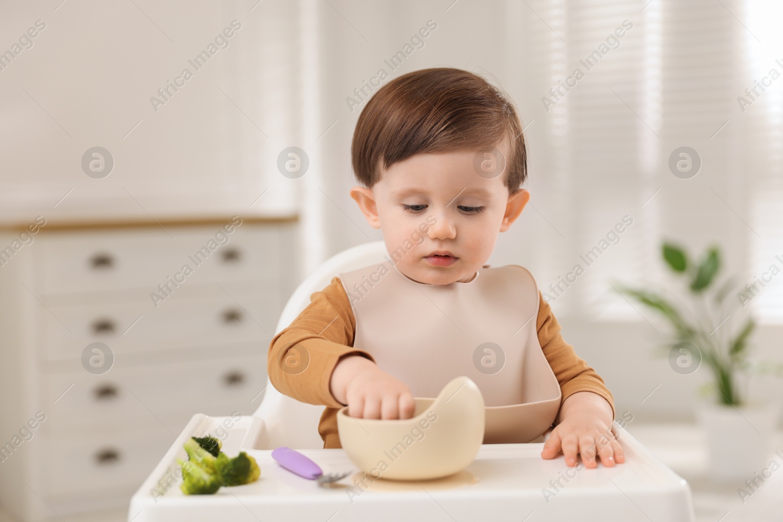 Photo of Cute little baby eating healthy food from bowl in high chair at home