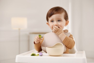 Photo of Cute little baby eating healthy food from bowl in high chair at home, space for text