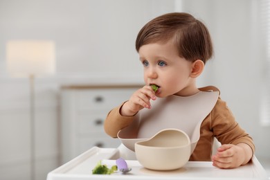 Photo of Cute little baby eating healthy food from bowl in high chair at home