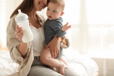 Mother holding cute little baby and bottle of milk on bed at home, selective focus. Space for text