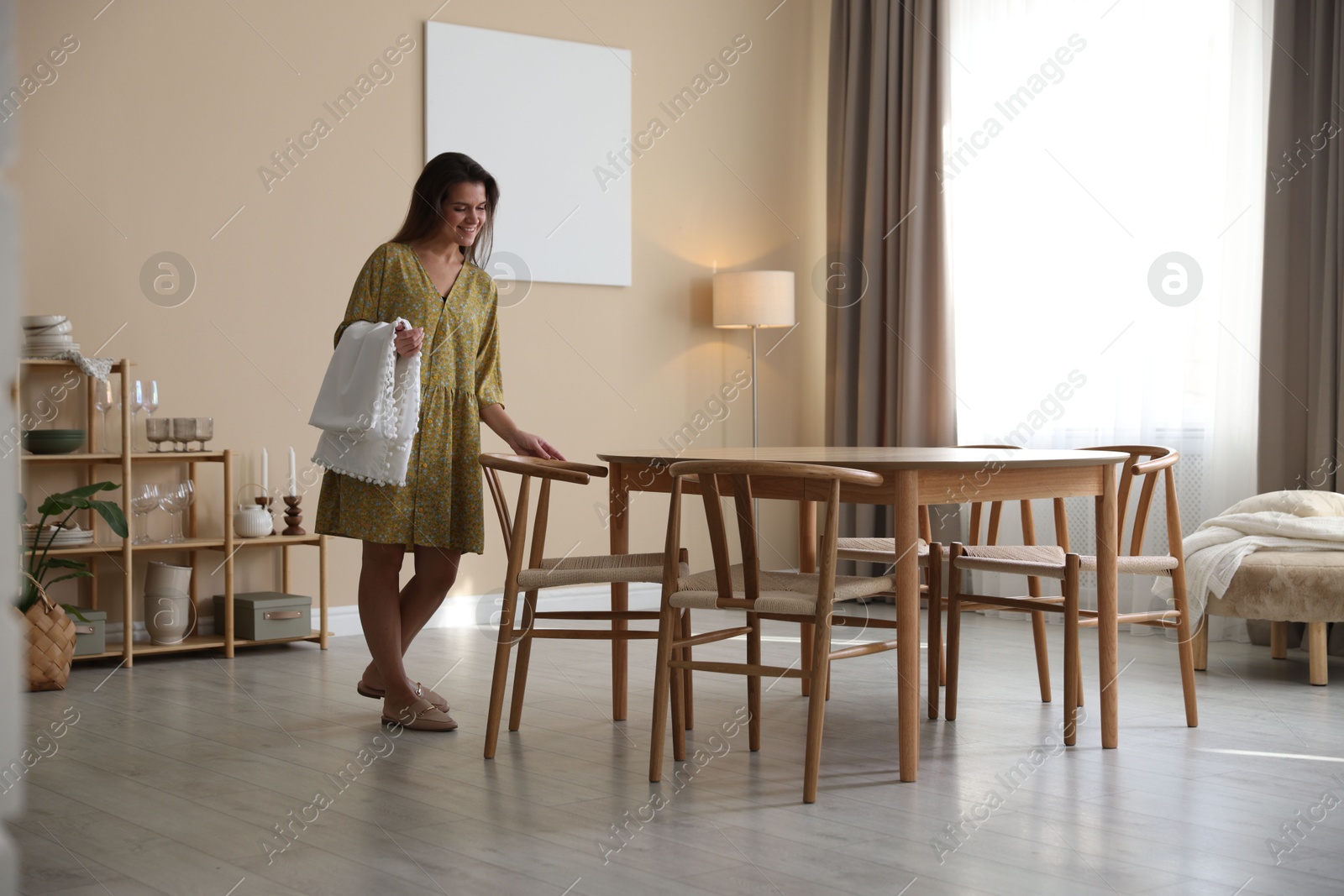 Photo of Woman with tablecloth and wooden chair near table at home