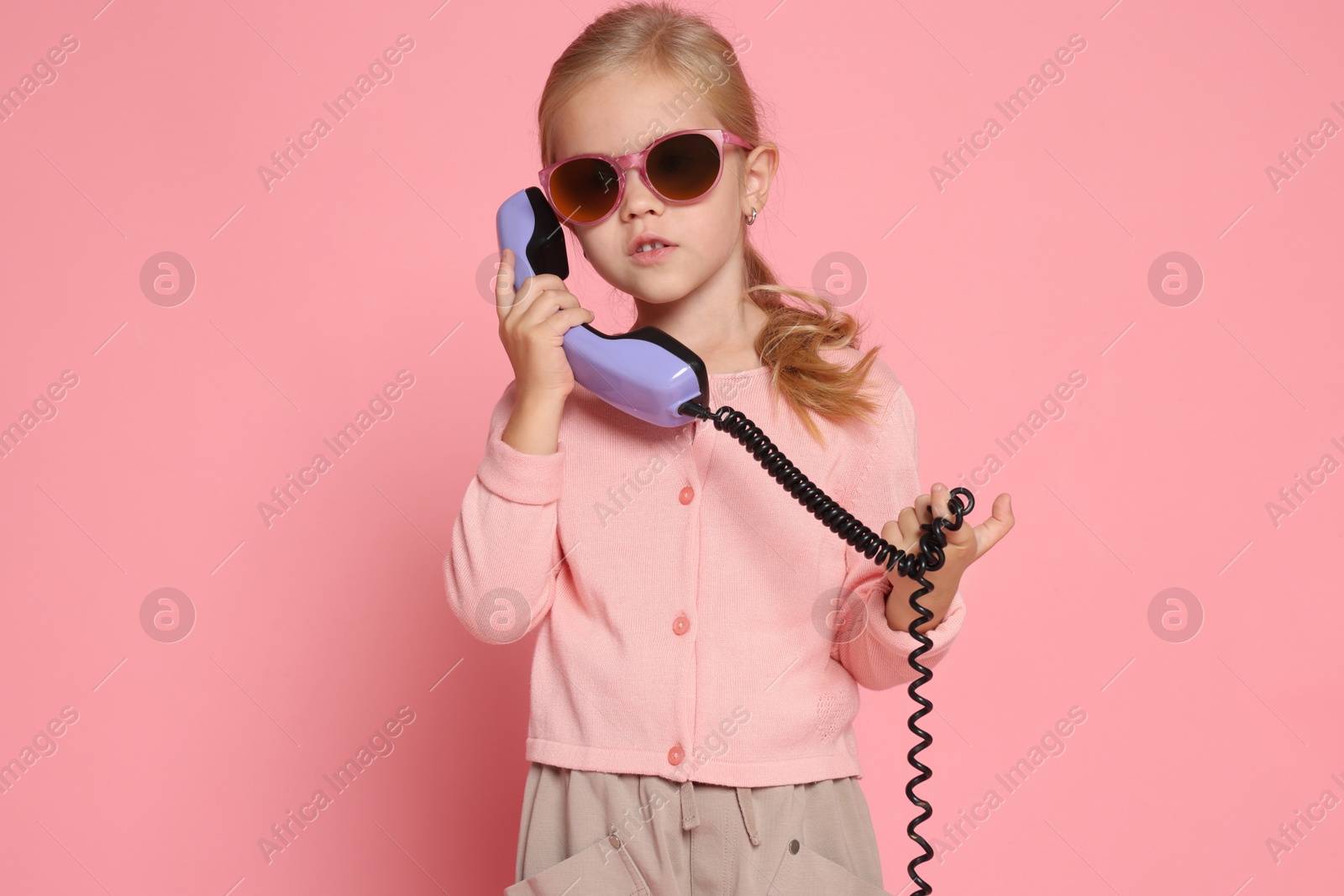 Photo of Cute little girl with handset of telephone on pink background