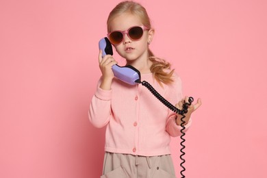 Cute little girl with handset of telephone on pink background