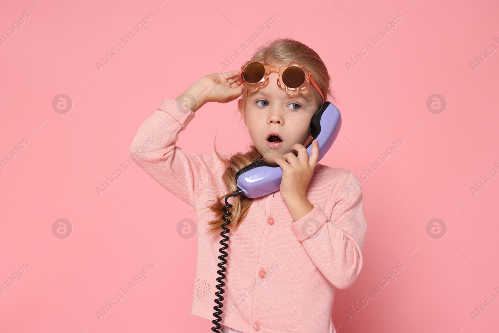 Photo of Cute little girl with handset of telephone on pink background