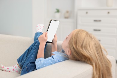 Cute little girl using smartphone on sofa at home