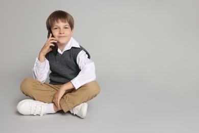 Photo of Cute little boy talking on smartphone against grey background, space for text