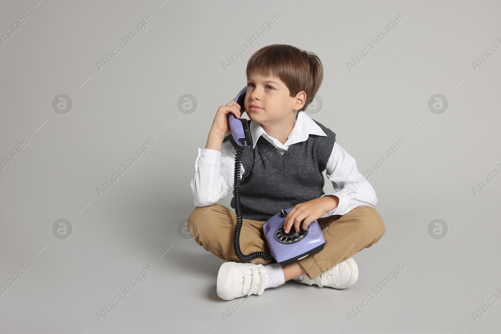 Photo of Cute little boy with old telephone on grey background