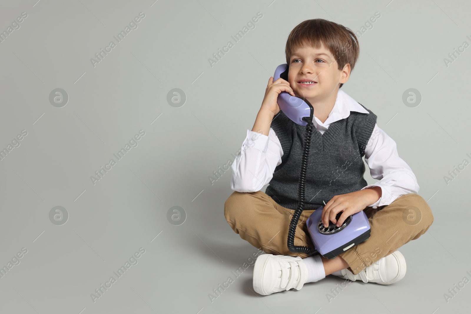 Photo of Cute little boy with old telephone on grey background, space for text