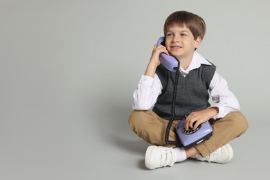 Cute little boy with old telephone on grey background, space for text