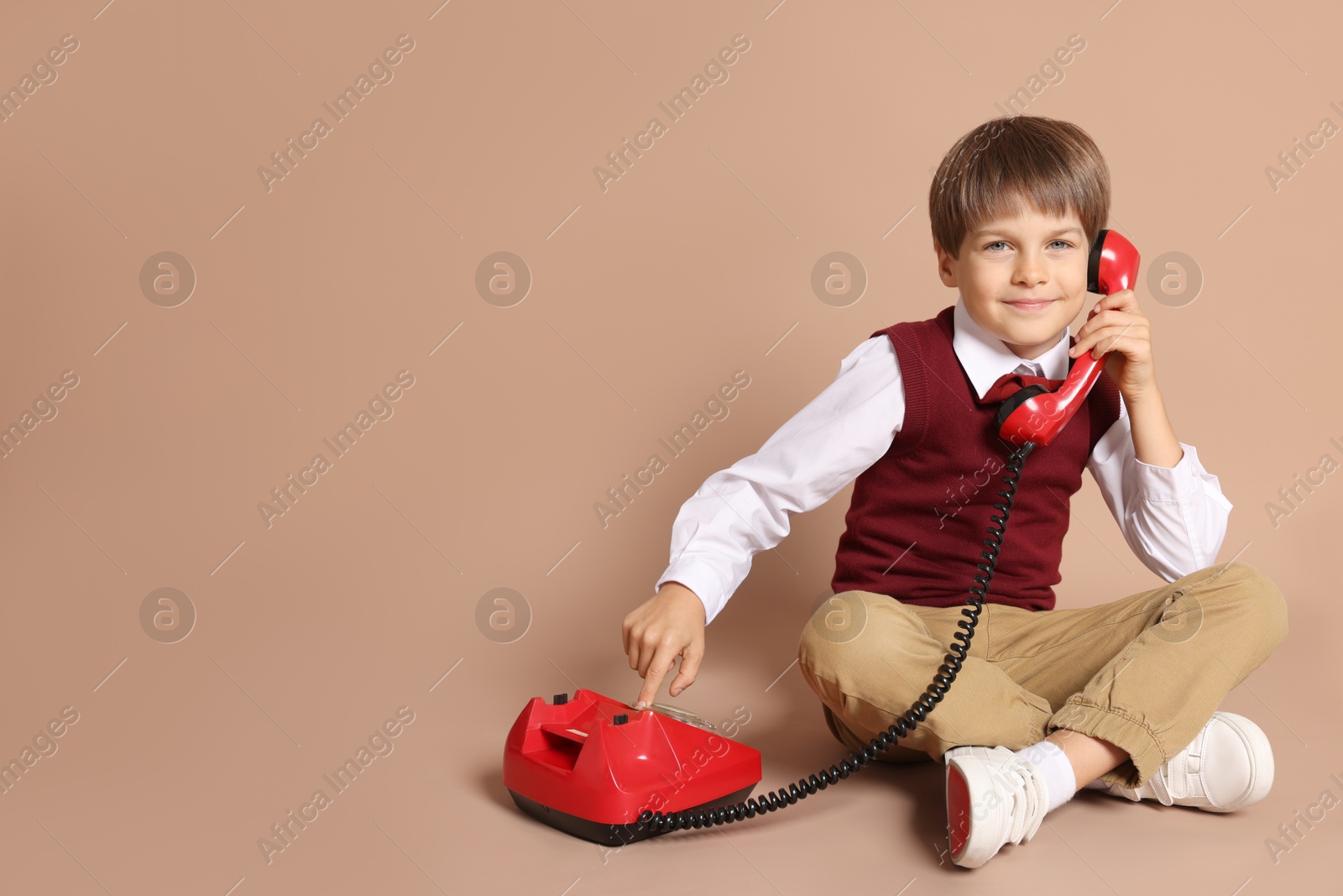 Photo of Cute little boy with old telephone on beige background, space for text