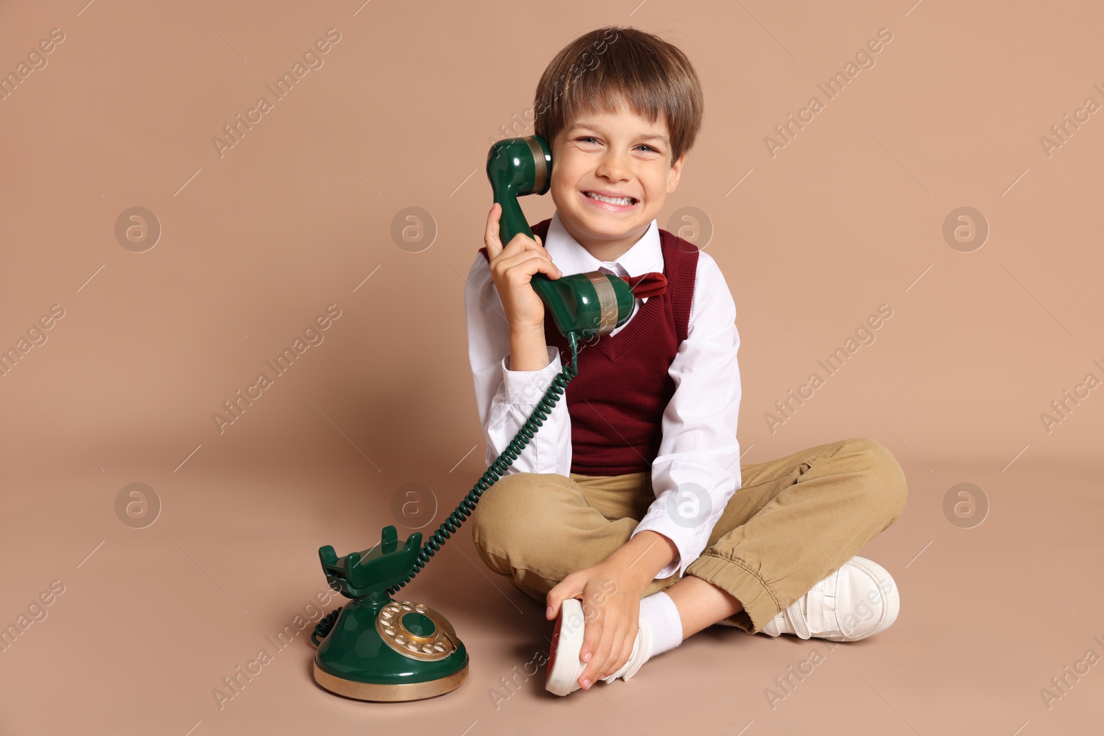 Photo of Cute little boy with old telephone on beige background