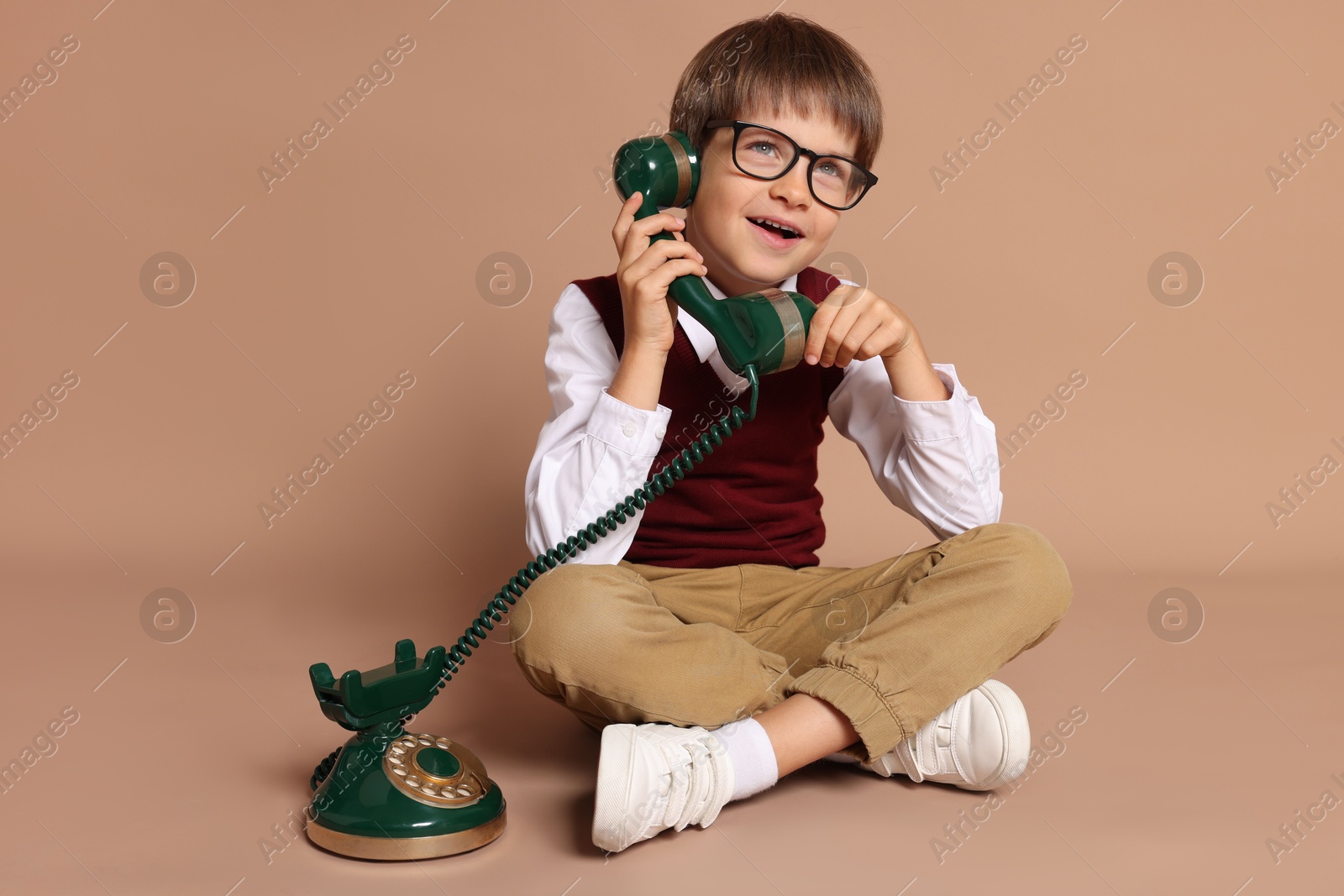 Photo of Cute little boy with old telephone on beige background