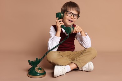 Cute little boy with old telephone on beige background