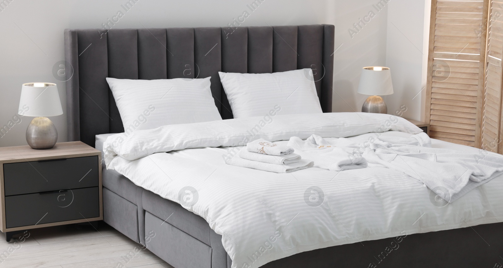 Photo of Bed with clean linens, pillows, towels and bathrobe indoors