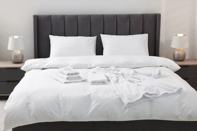 Photo of Bed with clean linens, pillows, towels and bathrobe indoors