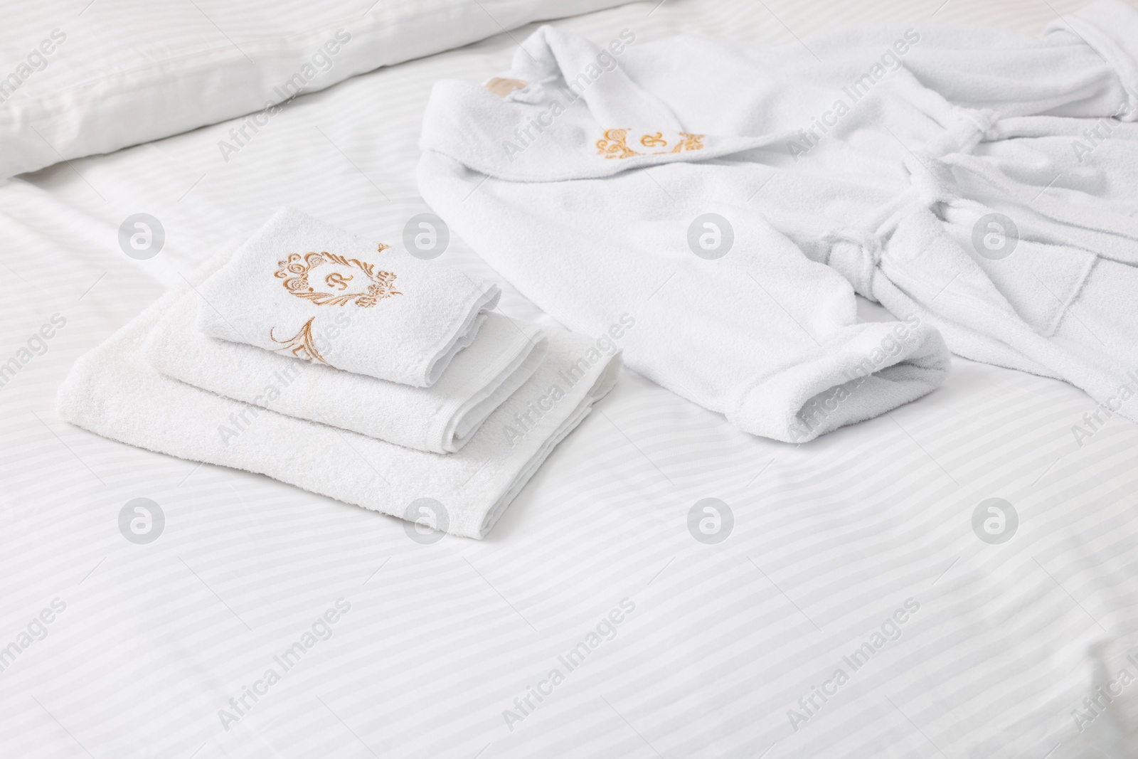 Photo of Bed with clean linens, towels and bathrobe indoors