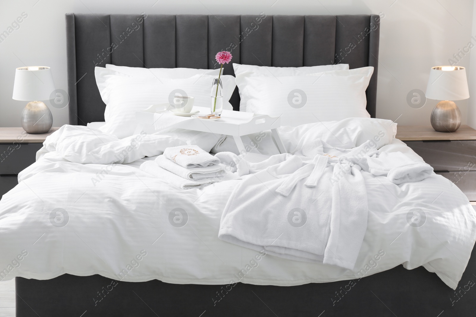 Photo of Breakfast tray, towels and bathrobe on bed with beautiful linens indoors