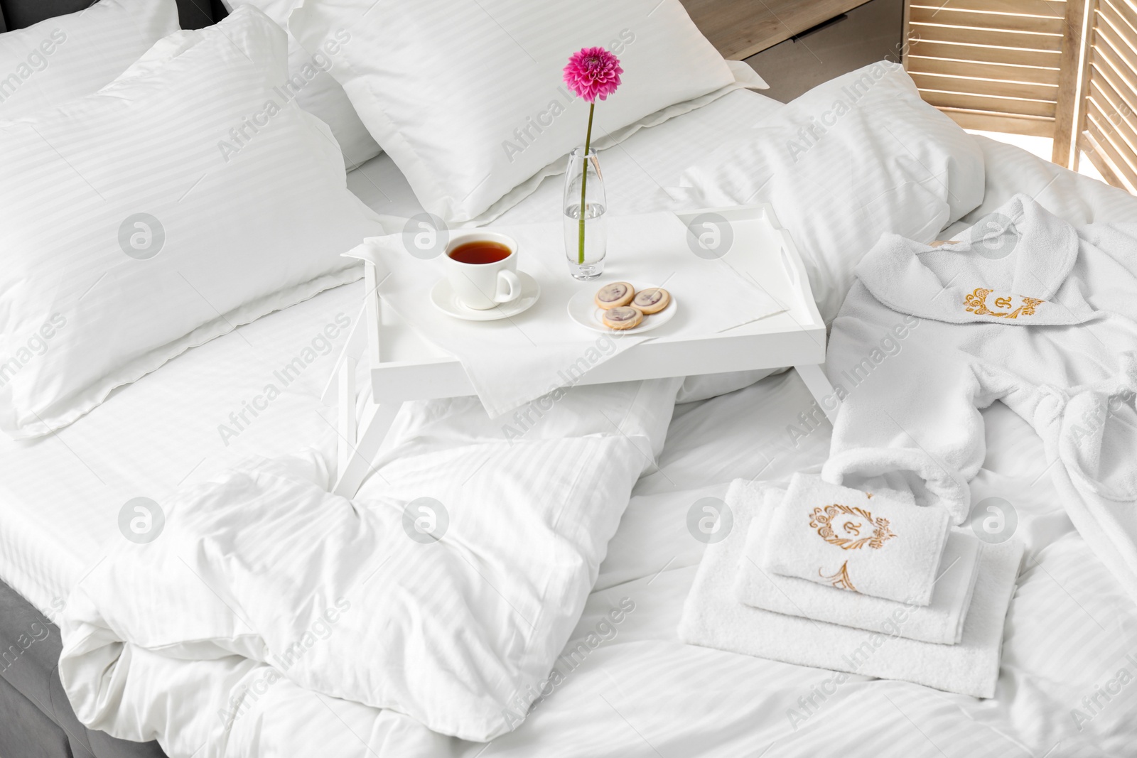 Photo of Breakfast tray, towels and bathrobe on bed with beautiful linens indoors