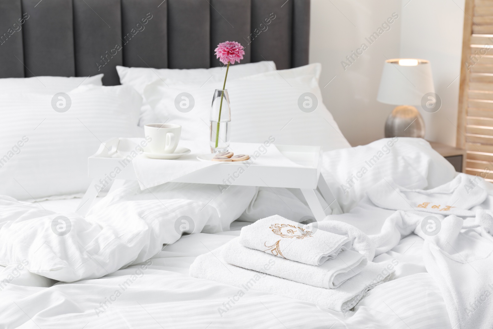 Photo of Breakfast tray, towels and bathrobe on bed with beautiful linens indoors