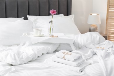 Photo of Breakfast tray, towels and bathrobe on bed with beautiful linens indoors