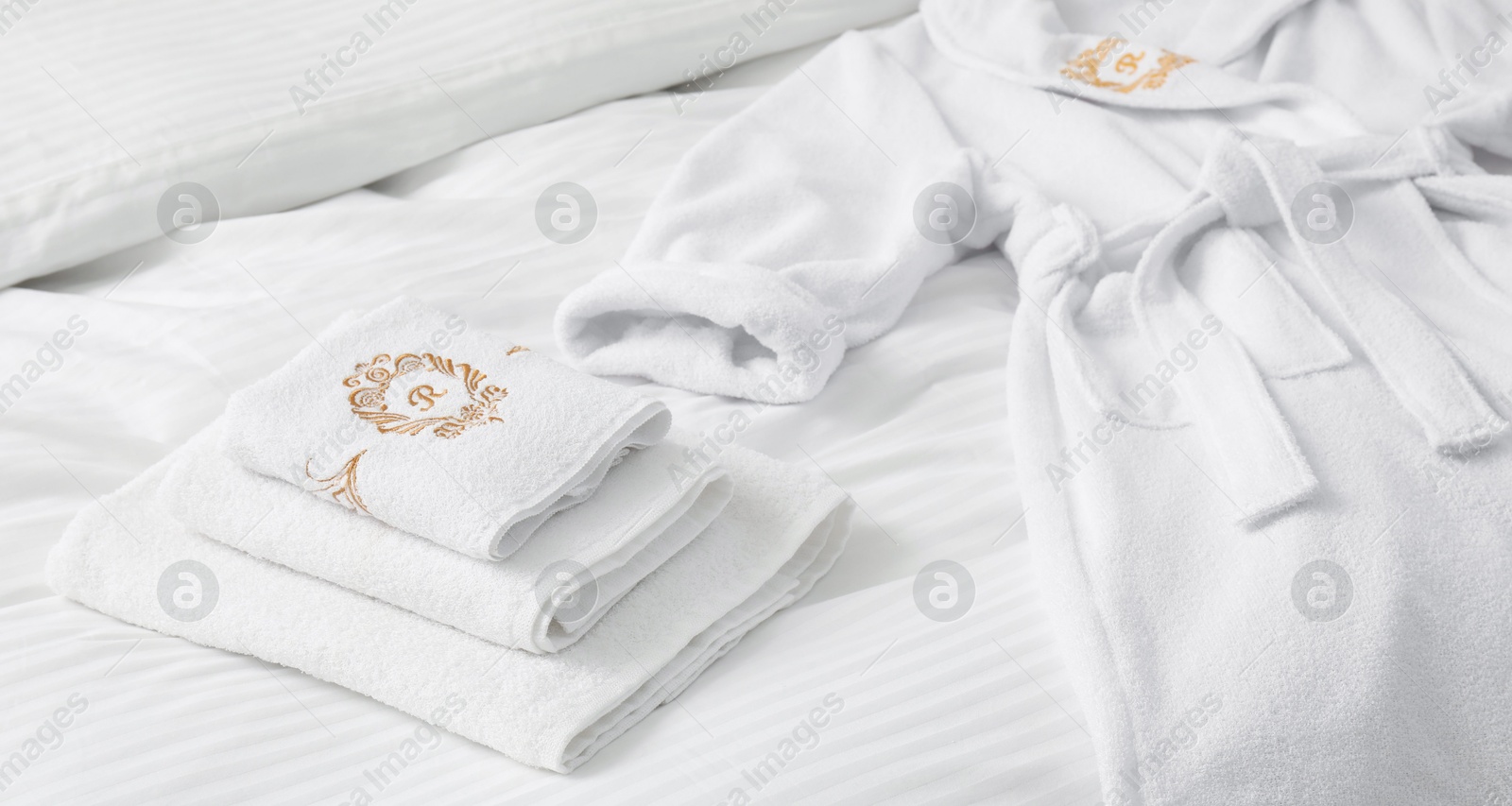 Photo of Comfortable bed with clean linens, pillows, towels and bathrobe indoors