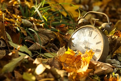 Photo of Autumn time. Vintage clock on fallen leaves in park, closeup with space for text