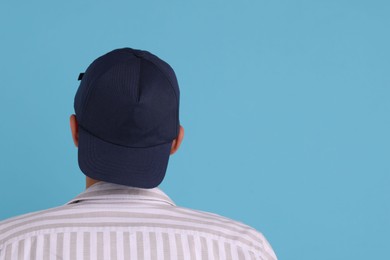 Photo of Man in stylish baseball cap on light blue background, back view. Mockup for design