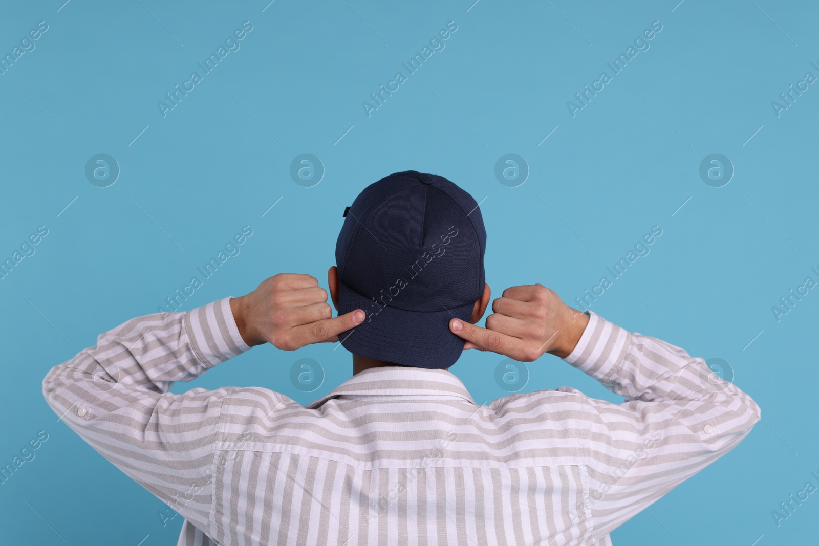 Photo of Man in stylish baseball cap on light blue background, back view. Mockup for design