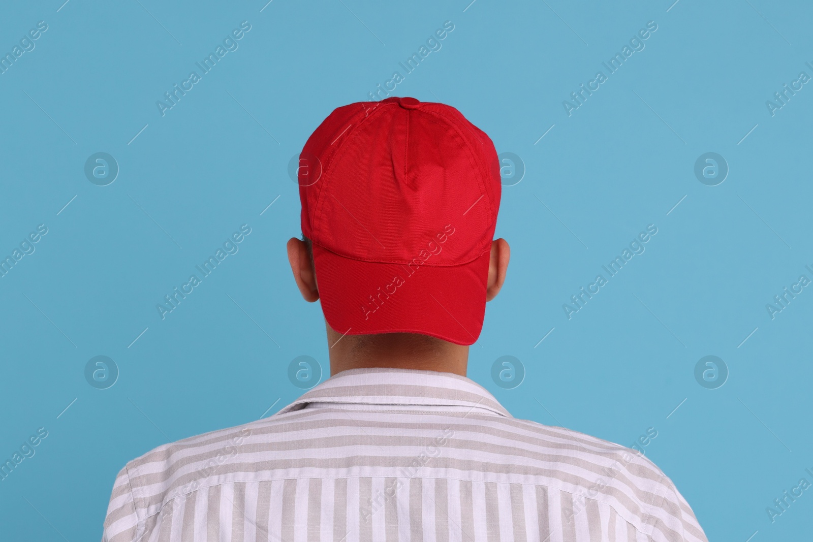 Photo of Man in stylish baseball cap on light blue background, back view. Mockup for design