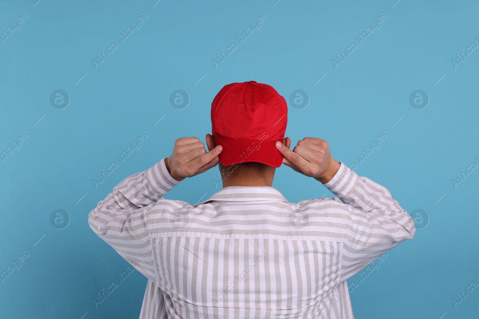 Photo of Man in stylish baseball cap on light blue background, back view. Mockup for design