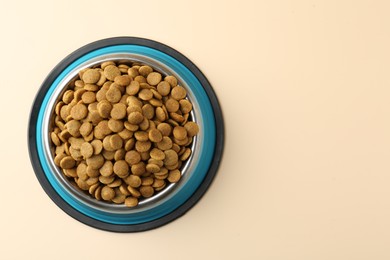 Photo of Dry pet food in feeding bowl on beige background, top view. Space for text