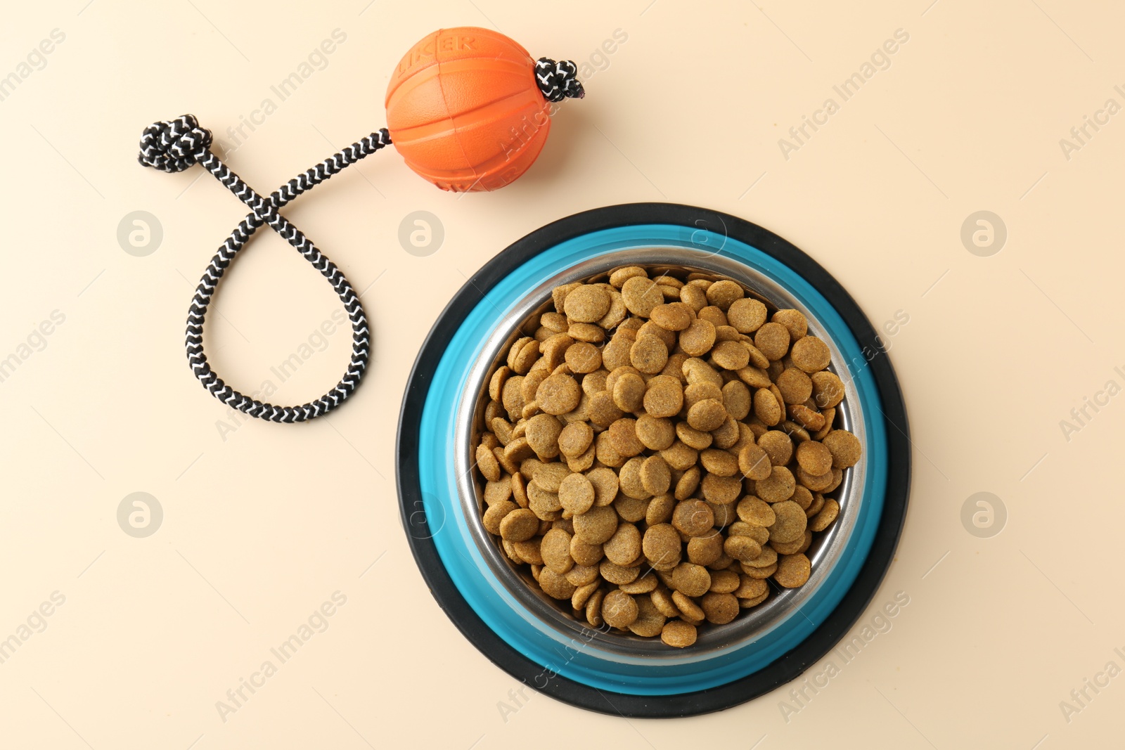 Photo of Dry pet food in feeding bowl and toy on beige background, flat lay