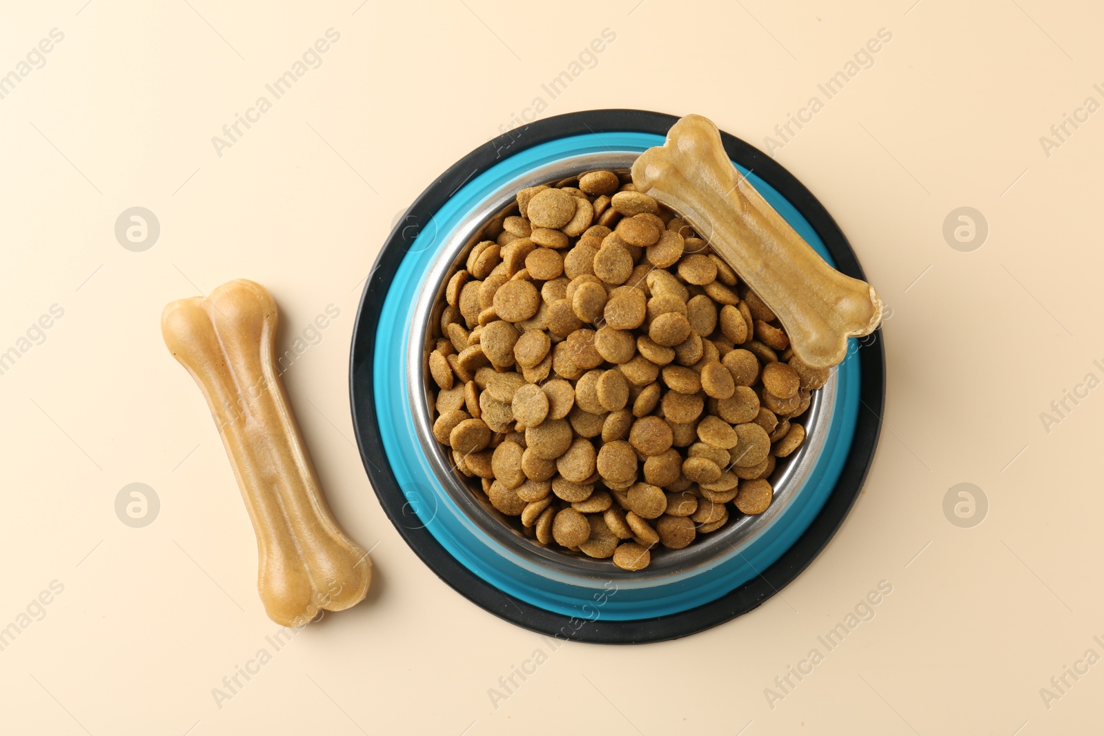 Photo of Dry pet food in feeding bowl and chew bones on beige background, top view