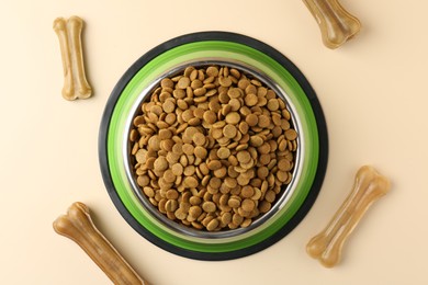 Photo of Dry pet food in feeding bowl and chew bones on beige background, top view